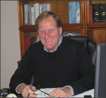 Mark Penfold at his desk, in front of the office bookshelves